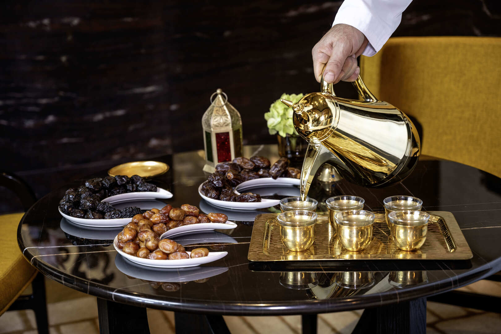 Traditional Arabic coffee being poured from a golden dallah into cups, served alongside an elegant assortment of dates on a black marble table at Banyan Tree Dubai.